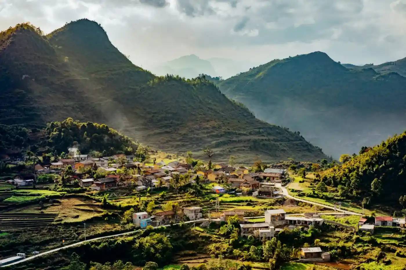 A village below steep green mountains at sunset in Ha Giang