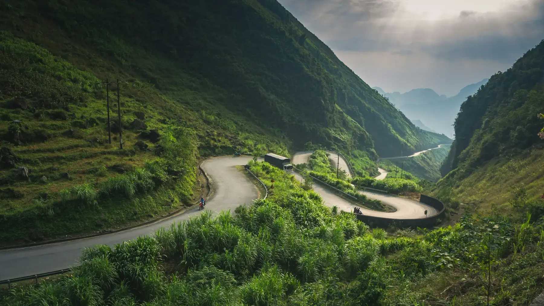 A road winding through a green valley in Ha Giang